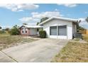 A single-story home with an attached garage and long driveway surrounded by lush greenery and a bright blue sky at 10309 Honeysuckle Ln, Port Richey, FL 34668