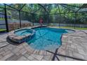 Relaxing screened-in pool area with a spa and waterfall feature, surrounded by a brick patio and lush greenery at 12800 Solola Way, Trinity, FL 34655