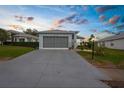 A light blue single-story home features a large driveway, gray roof, gray garage door, and manicured landscaping under a sunset sky at 18209 Breland Dr, Hudson, FL 34667