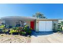 Charming single-story home featuring a red front door, attached garage and lovely garden in front of the home at 5316 Drift Tide Dr, New Port Richey, FL 34652