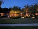 Exterior home elevation at night featuring exterior uplighting and tropical landscaping at 663 Turnberry Ct, Tarpon Springs, FL 34688