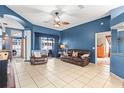 Comfortable living room with blue walls, tile flooring, ceiling fan, and sliding glass doors to the pool at 12040 Penzance Ln, New Port Richey, FL 34654