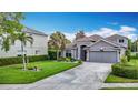 Inviting gray home boasts mature palm trees, lush landscaping, and a wide driveway leading to a two-car garage at 4207 Fishermans Lake Dr, Lutz, FL 33558