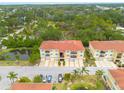Aerial view showcases condos with red roofs and balconies near a pond and wooded area, offering serene living at 5041 Royal Palms Way # 203, New Port Richey, FL 34652