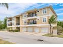 Exterior shot of a tan condo building with balconies and garages surrounded by lush green landscaping at 5041 Royal Palms Way # 203, New Port Richey, FL 34652