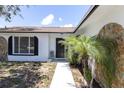 Inviting home featuring a stucco exterior, a black front door, and a well-maintained lawn and garden at 1402 Tallahassee Dr, Tarpon Springs, FL 34689