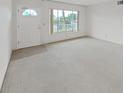 An empty sunlit living room with neutral carpet, a bright window and white front door at 2402 Ecuadorian Way # 40, Clearwater, FL 33763