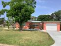 Charming single-story home with an attached garage, lush green lawn, and mature trees in a desirable neighborhood at 406 Driftwood E Dr, Palm Harbor, FL 34683
