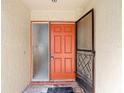 Close-up of a vibrant orange front door with adjacent glass panel and decorative screen door at 4420 Marine Pkwy, New Port Richey, FL 34652