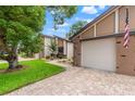 A home with a brick driveway and garage, with manicured lawn, trees, and flower beds at 7512 Heather Walk Dr, Weeki Wachee, FL 34613