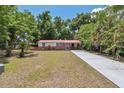 Inviting single-story home with a long driveway, red metal roof, and lush green trees in the background at 9306 21St, Tampa, FL 33612