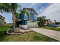 Two-story blue home featuring a large two-car garage, well-manicured lawn, and beautiful palm trees at 14008 Lugano Ct, Hudson, FL 34669