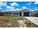Charming gray single-story home with a dark front door and garage door under a bright, cloudy sky at 6306 Aberdeen Ave, New Port Richey, FL 34653