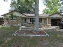 Inviting home with rock facade, featuring a well-kept yard with a mature tree and decorative landscaping at 7421 Fairfax Dr, Port Richey, FL 34668