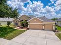 Inviting tan-colored single-story home with three-car garage, surrounded by a lush green lawn and blue skies at 13248 Linzia Ln, Spring Hill, FL 34609