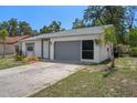 Single-story home with a grey two-car garage, well-maintained lawn, and mature trees around the house at 13307 Woodward Dr, Hudson, FL 34667