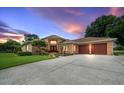 Exterior view of home featuring a brick facade, a two-car garage, well-maintained lawn, and dusk sky at 10044 Twelve Oaks Ct, Weeki Wachee, FL 34613