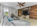 Cozy living room featuring a wood accent wall, large windows, a comfortable sectional sofa, and a ceiling fan at 1236 Ketzal Dr, Trinity, FL 34655