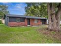 Exterior view of brick home with dark trim, a well-manicured lawn, and mature shade trees at 5323 23Rd St, Zephyrhills, FL 33542