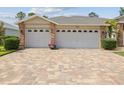 Three-car garage with brick accents and a colorful brick paver driveway at 18845 Fairway Green Dr, Hudson, FL 34667