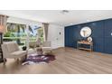 Bright living room with wood-look flooring, decor wall, and large window with lush landscaping view at 10224 Old Orchard Ln, Port Richey, FL 34668