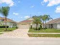 Well-maintained single-story home boasts a brick driveway, and lush landscaping with mature palm trees at 8457 Southern Charm Cir, Brooksville, FL 34613