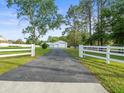 View of long asphalt drive, garages, white perimeter fence and meticulously maintained grounds at 15430 Oakcrest Cir, Brooksville, FL 34604