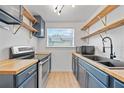 Galley kitchen with butcher block countertops, stainless steel appliances, blue cabinets, and floating wooden shelves at 4622 Paloverde Dr, New Port Richey, FL 34652