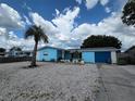 Charming blue single-story home with a gravel yard, mature trees, and a palm tree at 3252 Columbus Dr, Holiday, FL 34691