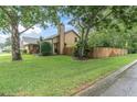 Exterior view of a home's side yard, showcasing mature trees, a wooden fence, and lush green grass at 7230 Hummingbird Ln, New Port Richey, FL 34655
