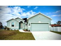 Charming one-story house with a light teal exterior, two-car garage, and landscaped lawn at 1590 Royal Rd, Venice, FL 34293