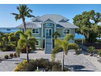 Two-story waterfront home with metal roof, paver driveway, and lush landscaping at 1910 Oregon Trl, Englewood, FL 34224