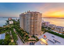 An aerial view showcases a luxury high-rise building, tropical landscaping, and waterfront views at sunset at 35 Watergate Dr # 503, Sarasota, FL 34236