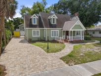 Charming green home featuring a welcoming front porch, brick driveway, and well-maintained landscaping at 7754 Westmoreland Dr, Sarasota, FL 34243