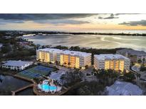 Beautiful aerial view of condos with a serene waterfront, pool, and tennis courts at sunset at 280 Hidden Bay Dr # 302, Osprey, FL 34229
