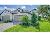 Two-car garage, paver driveway, and landscaped lawn with lush greenery at 100 Corserra Dr, Nokomis, FL 34275