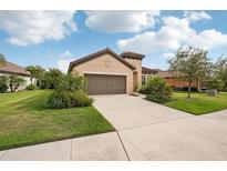 Single-story house with a two-car garage, landscaping, and a light brown exterior at 308 Cassano Dr, Nokomis, FL 34275