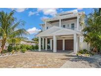 Two-story home with white exterior, two-car garage, and a brick driveway at 404 North Shore Dr, Anna Maria, FL 34216