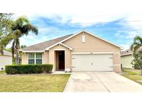 Tan single-story home with a two car garage, manicured lawn, and a palm tree at 7380 Mikasa Dr, Punta Gorda, FL 33950