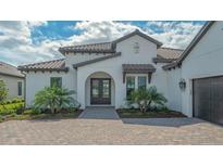 Charming white home exterior featuring a tile roof, arched entry, and professionally landscaped front yard at 10629 Nicklaus Ct, Englewood, FL 34223