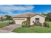 Tan one-story house with a two-car garage and landscaped yard at 1480 Mossy Oak Dr, North Port, FL 34287