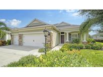 House exterior featuring a three-car garage, stone accents and a manicured lawn at 16916 Rosedown Gln, Parrish, FL 34219