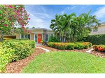 Charming home with lush landscaping, including palm trees, colorful flowers, and a vibrant orange front door at 136 Crescent Dr, Anna Maria, FL 34216