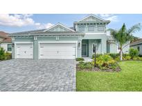 Two-story home with light teal exterior, three car garage, and landscaping at 12420 Destin Loop, Venice, FL 34293