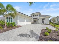 Beautiful home featuring a three-car garage, light exterior, and paver driveway surrounded by lush landscaping at 8332 Sea Glass Ct, Sarasota, FL 34240