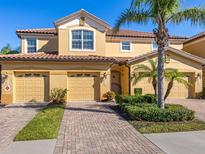 Tan two-story home with two-car garage, lush landscaping, and brick paver driveway at 8133 Miramar Way # 201, Lakewood Ranch, FL 34202