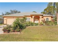 Tan house with gray roof, two-car garage, and landscaped yard at 3623 Monday Ter, North Port, FL 34286