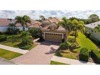 Inviting single-Gathering home featuring a terracotta roof, brick driveway, lush landscaping, and a two-car garage at 1330 Still River Dr, Venice, FL 34293