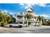 Elegant two-story home boasts balconies, palm trees, and a pristine white exterior, creating a luxurious tropical ambiance at 598 Lyons Ln, Longboat Key, FL 34228