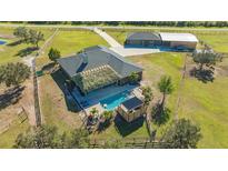 Aerial view of home with a backyard pool and a tiki hut, surrounded by a lush green lawn and mature trees at 25205 67Th E Ave, Myakka City, FL 34251